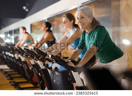 Portrait of active mature woman training on stationary bike workout in gym