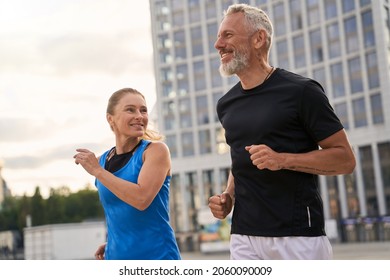 Portrait of active middle aged couple, man and woman in sportswear looking happy while jogging together outdoors, having mroning workout - Shutterstock ID 2060090009
