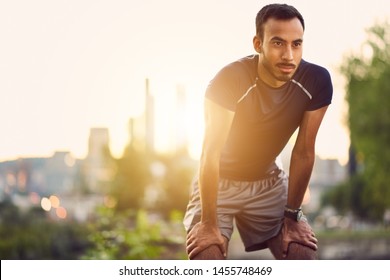 Portrait Of Active Millenial Man Jogging At Dusk With An Urban Cityscape And Sunset In The Background