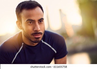 Portrait Of Active Millenial Man Jogging At Dusk With An Urban Cityscape And Sunset In The Background