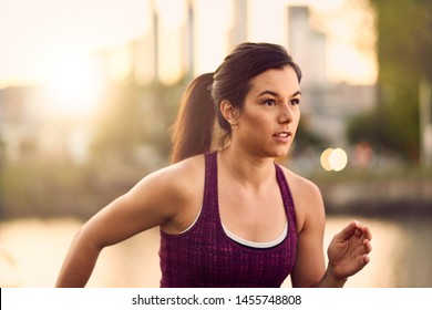 Portrait Of Active Millenial Woman Jogging At Dusk With An Urban Cityscape And Sunset In The Background