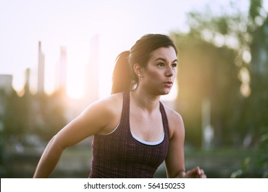 Portrait Of Active Millenial Woman Jogging At Dusk With An Urban Cityscape And Sunset In The Background