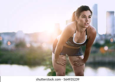 Portrait of active millenial woman jogging at dusk with an urban cityscape and sunset in the background - Powered by Shutterstock