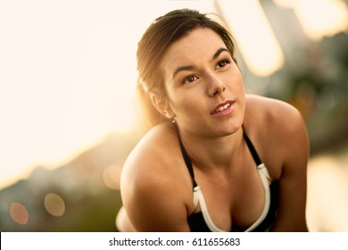 Portrait Of Active Millenial Woman Jogging At Dusk With An Urban Cityscape And Sunset In The Background