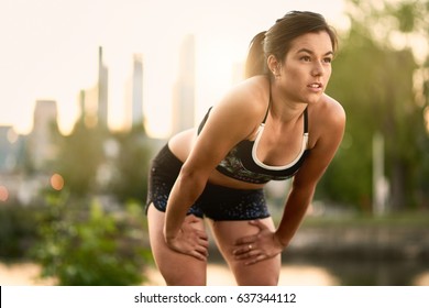 Portrait Of Active Millenial Woman Jogging At Dusk With An Urban Cityscape And Sunset In The Background