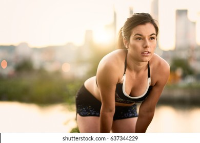 Portrait Of Active Millenial Woman Jogging At Dusk With An Urban Cityscape And Sunset In The Background