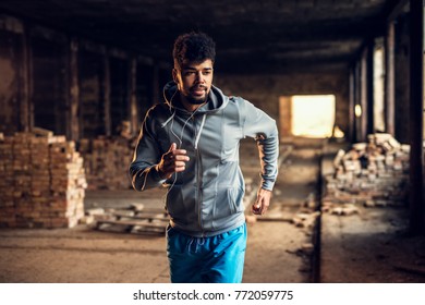 Portrait of active motivated afro-american young attractive athletic man with earphones running inside of the abandoned place.