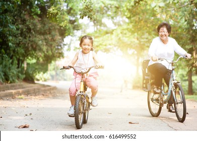 Portrait of active multi generations Asian family at nature park. Grandmother and granddaughter riding bicycle outdoor. Morning sun flare background. - Powered by Shutterstock