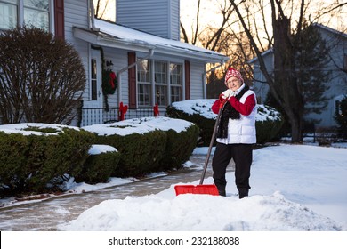 Portrait Of Active Senior Citizen With Snow Shovel In Front Of Home