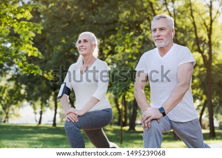 Portrait of active senior couple doing warm up exercises while standing in park outdoors
