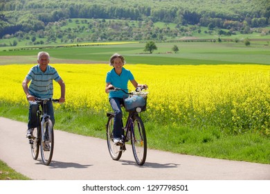 Portrait of active senior couple riding bike on road in countryside Stock Photo