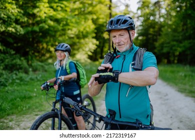 Portrait of active senior couple riding bicycles at summer park, looking at sports smartwatch, checking their performance. - Powered by Shutterstock