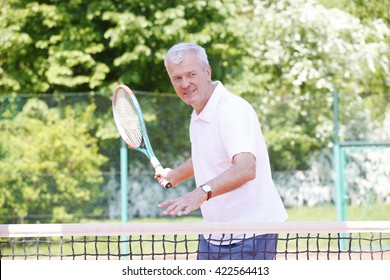 Portrait Of Active Senior Man With Tennis Racket Serving On Court.