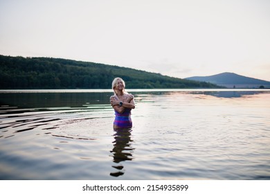 Portrait of active senior woman swimmer standing and splashing outdoors in lake.
