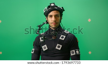 Portrait of an Actor Wearing Motion Caption Suit and Head Rig Posing with Green Screen Background. Film Studio Set Shooting Blockbuster Movie with Chroma Key. Medium Shot Looking at Camera