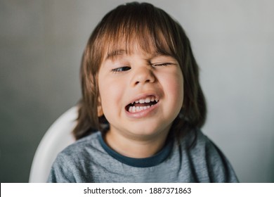 Portrait Of Adorable 3 Year Old Kid Learning To Wink His Eye. Cute Caucasian Boy With Funny Face Expression. Real Child Having Fun Indoors With Family. Healthy And Happy Childhood. Parenting Concept.