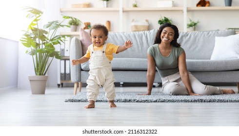 Portrait Of Adorable African American Infant Boy Making His First Steps At Home, Cute Little Black Toddler Child Wearing Jumpsuit Walking In Living Room, His Happy Mom Smiling On Background, Panorama - Powered by Shutterstock