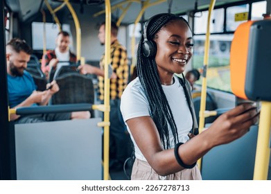 Portrait of an adorable african american joyful woman standing on the bus and using the phone to buy a ticket. Public transportation, technology and people concept.Copy space. - Powered by Shutterstock