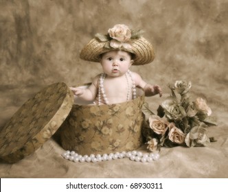 Portrait Of An Adorable Baby Girl Playing Dress Up, Sitting In A Hatbox Wearing A Straw Hat And Pearl Necklace