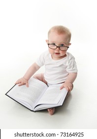 Portrait of an adorable baby sitting up wearing eyeglasses and looking at a book, isolated on white