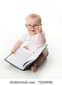 Portrait of an adorable baby sitting up wearing eyeglasses and looking at a book, isolated on white