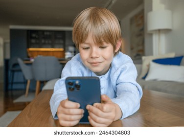 Portrait of adorable caucasian boy using smartphone lying on a table at home - Powered by Shutterstock