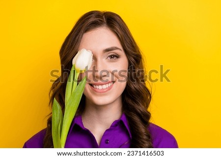 Portrait of adorable cheerful person beaming smile tulip flower cover one eye isolated on yellow color background
