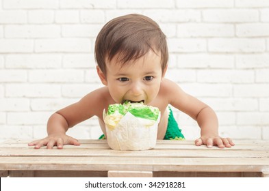 portrait of adorable handsome toddler eating sponge cake with white walls on background