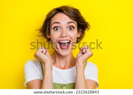 Portrait of adorable impressed woman with bob hairstyle dressed khaki overall open mouth clench fists isolated on yellow color background
