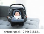 Portrait of adorable less than one month old newborn baby girl sleeping in the modern car seat with fastening safety belt at home. Selective focus on little Asian Australian child