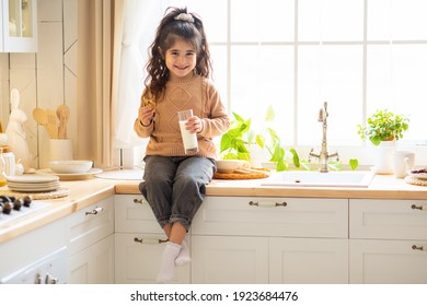 Portrait Of Adorable Little Arab Girl Eating Cookies And Drinking Milk In Kitchen, Cute Female Child Enjoying Healthy Snack At Home, Preschool Kid Sitting At Table And Smiling At Camera, Copy Space