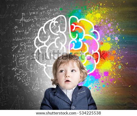 Portrait of an adorable little boy wearing a suit and standing near a chalkboard with a colorful brain sketch. Concept of child's development