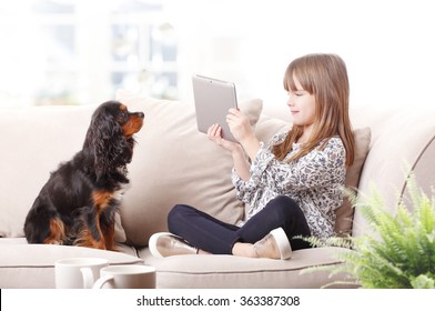 Portrait of adorable little girl holding in hand a digital tablet and taking picture while her cute pet lying next to her. Arkistovalokuva