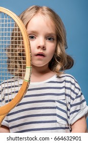 Portrait Of Adorable Little Girl Holding Tennis Raquet And Looking At Camera Isolated On Blue