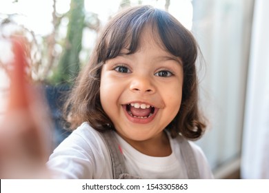 Portrait of an adorable little girl taking a selfie while playing in her living room at home - Powered by Shutterstock