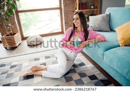 Portrait of adorable pretty girlish person with stylish hairstyle wear pink blouse sit on floor holding cup of coffee at home indoors