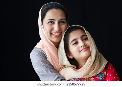 Portrait Of Adorable Smiling Pakistani Muslim Girl With Beautiful Eyes And Her Mother Wearing Hijab In Traditional Dress On Dark Black Background, Warm Love In Happy Islamic Family Of Mom And Daughter