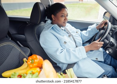 Portrait Of Adult Black Woman Driving Car With Grocery Bag In Foreground After Shopping In Supermarket