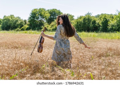 Portrait of adult caucasian female in the wheat field holding violin - Woman in summer day dancing alone outdoor full length back view - freedom nature solitude mother nature concept - Shutterstock ID 1786942631