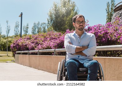 Portrait Of Adult Caucasian Hispanic Latino Man, With Beard And Glasses, Serious In A Wheelchair Looking At The Camera, Outdoors In A Nice Park