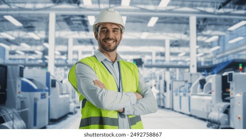 Portrait of Adult Caucasian Male Production Supervisor Looking at Camera And Smiling. Technician in a Hardhat And Reflective Jacket at an Industrial Factory with Heavy Machinery Producing Electronics. - Powered by Shutterstock