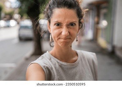 Portrait of adult caucasian woman stand in town or city outdoor in day mad frowning