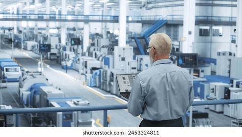 Portrait of an Adult Engineer Standing on a Platform, Using Laptop Computer at an Electronics Factory. Technician Making Technical Upgrades Online Over an Internet Software - Powered by Shutterstock