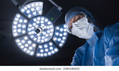 Portrait of adult female surgeon at work. Concentrated female surgeon wearing protective blue gown and face mask doing operation, surgery. Microsurgery treatment - Powered by Shutterstock