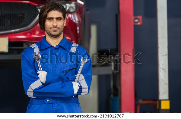Portrait adult handsome male mechanic wearing\
uniform, crossed arms, posing with confidence, standing in garage\
at car or automobile maintenance service center or shop, copy\
space. Industry\
Concept