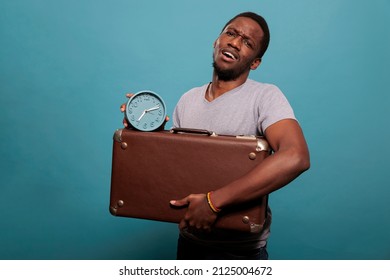 Portrait Of Adult Holding Suitcase And Clock In Front Of Camera, Preparing To Leave On Journey Trip. Casual Man With Briefcase Luggage Checking Time On Watch, Running Late On Vacation.