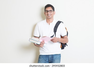 Portrait Of Adult Indian College Student With Bag And Books. Asian Man Standing On Plain Background With Shadow And Copy Space. Handsome Mixed Race Male Model.