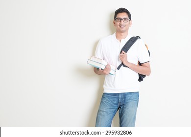 Portrait Of Adult Indian University Student With Books And Bag. Asian Man Standing On Plain Background With Shadow And Copy Space. Handsome Mixed Race Male Model.