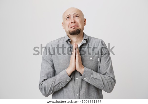 Portrait of adult male looking sad and miserable holding his hands in pray over white background. Poor man in casual clothes hopes that his wife would not find out about his mistress.