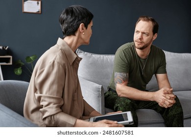 Portrait of adult man as army veteran talking to female psychologist and sharing mental health problems in therapy session - Powered by Shutterstock